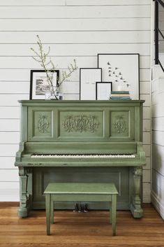 an old green piano in a room with pictures on the wall and a bench next to it