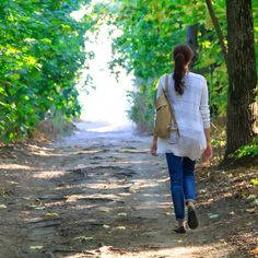 a woman walking down a dirt road in the woods