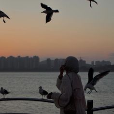 a person standing on a boat looking at birds flying in the air over water with buildings in the background