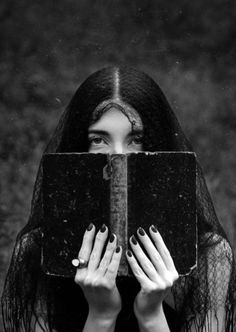 a woman with long black hair covering her face behind an open book in front of her face