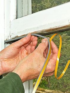 a person is holding a yellow ribbon in front of an open window with trees outside