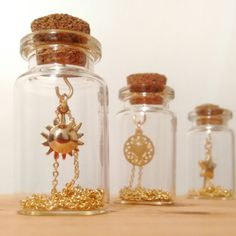 three glass jars with gold chains and charms in them sitting on a table next to each other