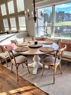 a dinning room table with four chairs and a bench in front of large windows