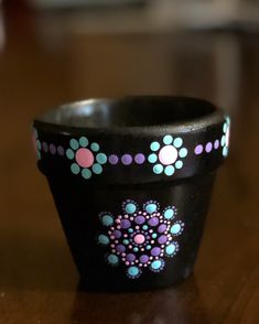 a black cup with pink, blue and green designs on it sitting on a table