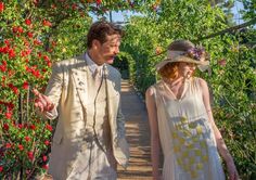 the man and woman are walking down the path in the flowered area with red flowers