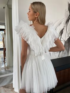 a woman standing in front of a painting wearing a white dress with ruffles