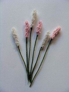 three pink and white flowers are on a white surface with some green stems in the foreground