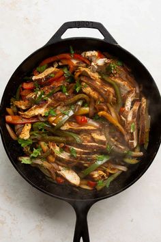 a skillet filled with chicken and vegetables on top of a white counter next to a wooden spoon