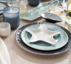 a table set with blue and white plates, silverware, candles and napkins