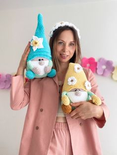 a woman is holding two crocheted gnomes