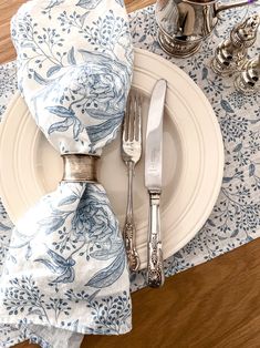 a place setting with blue and white napkins, silverware and a teapot