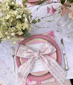 the table is set with pink and white plates, silverware, and floral centerpieces