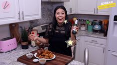 a woman holding a bottle and some food on a cutting board in a kitchen with white cabinets