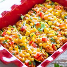 a red casserole dish filled with corn and tomatoes on a wooden table next to parsley