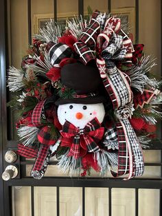 a christmas wreath with a snowman and plaid bow hanging on the front door,