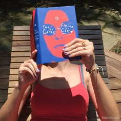 a woman sitting on top of a wooden bench holding a blue book over her face