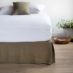 a bed with white sheets and pillows in a room next to a potted plant