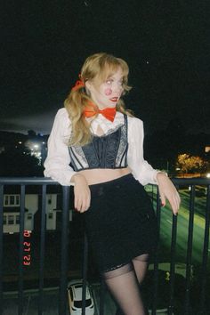 a woman dressed up as a clown standing on a balcony at night with her hands on her hips