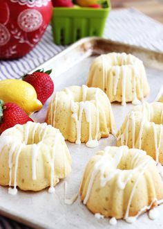 lemon bundts with icing on a baking sheet next to strawberries and lemons