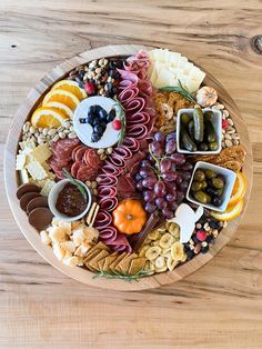 a wooden platter filled with different types of cheeses, crackers and fruit