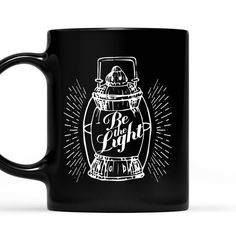 a black coffee mug with the words be the light and an image of a bottle