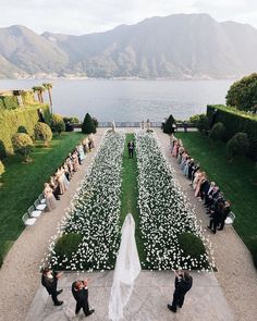 an aerial view of a wedding ceremony in front of a lake with flowers on the lawn