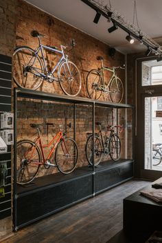 there are many bikes on display in the store window and behind them is a brick wall with several bicycles mounted to it