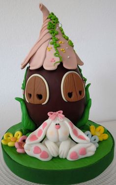 a cake that is shaped like a house and has bunny ears on the roof, with flowers around it