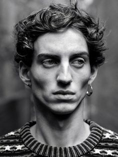 a black and white photo of a young man with curly hair wearing a striped sweater