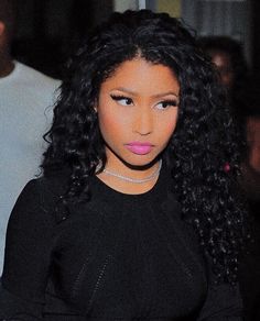 a close up of a person wearing a black shirt and long curly hair with pink lipstick