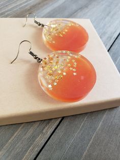 Beautiful and fiery sunset orange resin disk earrings, filled with gold stars. Vibrantly orange circle half circles, paired its clear stary other half, perfectly preserved in resin for it's natural beauty. Vividly colorful, lightweight, and dazzling stars in every light setting ♥ Be sure to check out the ORANGE EARRINGS section at EarringsbyLCreations for all beautiful orange colored earrings available! https://www.etsy.com/shop/EarringsByLCreations?section_id=28420987 Made with quality material Orange Resin Dangle Earrings, Orange Dangle Resin Earrings, Orange Resin Jewelry For Party, Orange Resin Earrings, Gold Star Earrings, Orange Earrings, Disc Earrings, Green Gems, Burlap Ribbon