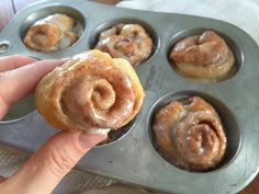 a person is holding a cinnamon roll in a muffin tin with other pastries