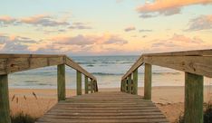 a wooden walkway leading to the beach at sunset