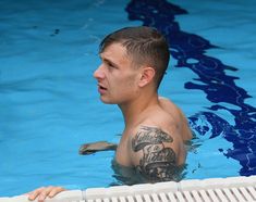 a man with a tattoo on his arm is in the water near a swimming pool