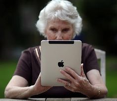 an older woman sitting at a table with her ipad in front of her, holding the screen