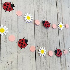 paper flowers and ladybugs are arranged on a wooden floor with white daisies