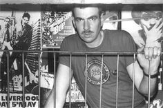 a man standing behind a metal fence with posters on the wall in the back ground