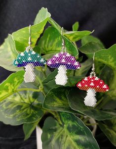 three different colored mushroom shaped earrings on top of a green leafy plant in front of a black background