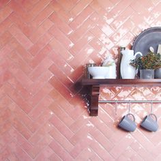 a shelf with pots and mugs on it in front of a pink tiled wall