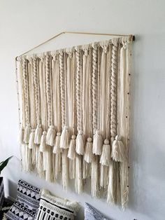 a wall hanging made out of yarn and tassels on a white wall next to a plant