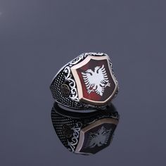 "Silver Albanian Eagle signet on the red pearl. There is illyrian shield symbol at the sides of the ring. Illyrians are considered to be the ancestors of the Albanian nation. This ring has Red Pearl Stone under the Albanian Double Head Eagle. I am designing a logo or symbol for you on the stone's empty area by use enamel work. Items has 1 year guaranty for the production mistakes. Stone: Red Pearl Material: Sterling Silver 925k and Bronze Plated: Rodium Plated Weight: 16.00gr Please make sure yo Collectible Red Engraved Ring, Red Symbolic Engraved Jewelry, Red Ring With Inlay, Red Inlay Ring, Red Inlay Ring Jewelry, Symbolic Red Jewelry For Anniversary, Red Inlay Rings For Gifts, Engraved Red Ring Jewelry, Engraved Red Round Signet Ring