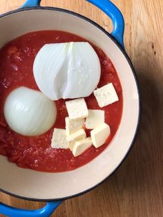 an onion, cheese and tomato soup in a blue pot on a wooden table top