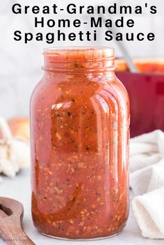 a jar filled with homemade spaghetti sauce on top of a white counter next to a wooden spoon