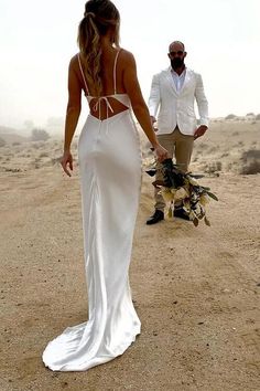 a man and woman walking in the desert with one wearing a white dress, holding hands