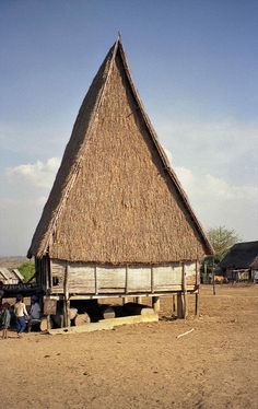 an old hut with thatched roof and people sitting on the ground in front of it