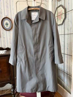 This classic overcoat is from London Fog, made from 65 per cent polyester and 35 per cent cotton in medium grey. It fastens with the original buttons in the front and has two front pockets, and it's fully lined with a beige, grey and black checked lining. Marked size 42 short. The measurements, taken with the coat lying flat, are: shoulder to shoulder, 19 inches; armpit to armpit, 22 inches; sleeves, 24 inches; length, 42 inches; bottom edge, 32 inches. In very good condition. Winter Gray Raincoat With Pockets, Classic Outerwear For Rainy Weather, Classic Outerwear For Rainy Season, Gray Cotton Business Outerwear, Gray Long Sleeve Outerwear For Rainy Weather, Classic Business Raincoat For Winter, Classic Winter Business Raincoat, Classic Long Single Breasted Raincoat, Classic Long Single-breasted Raincoat