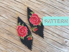 a pair of black and red beaded earrings with roses on them sitting on a wooden table