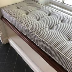 a striped mattress sitting on top of a wooden bench in front of a windowsill