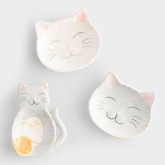 three ceramic dishes with cats on them and one has an orange in its mouth, the other has a cat's head