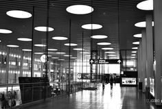 a black and white photo of people walking through an airport lobby with circular lights on the ceiling